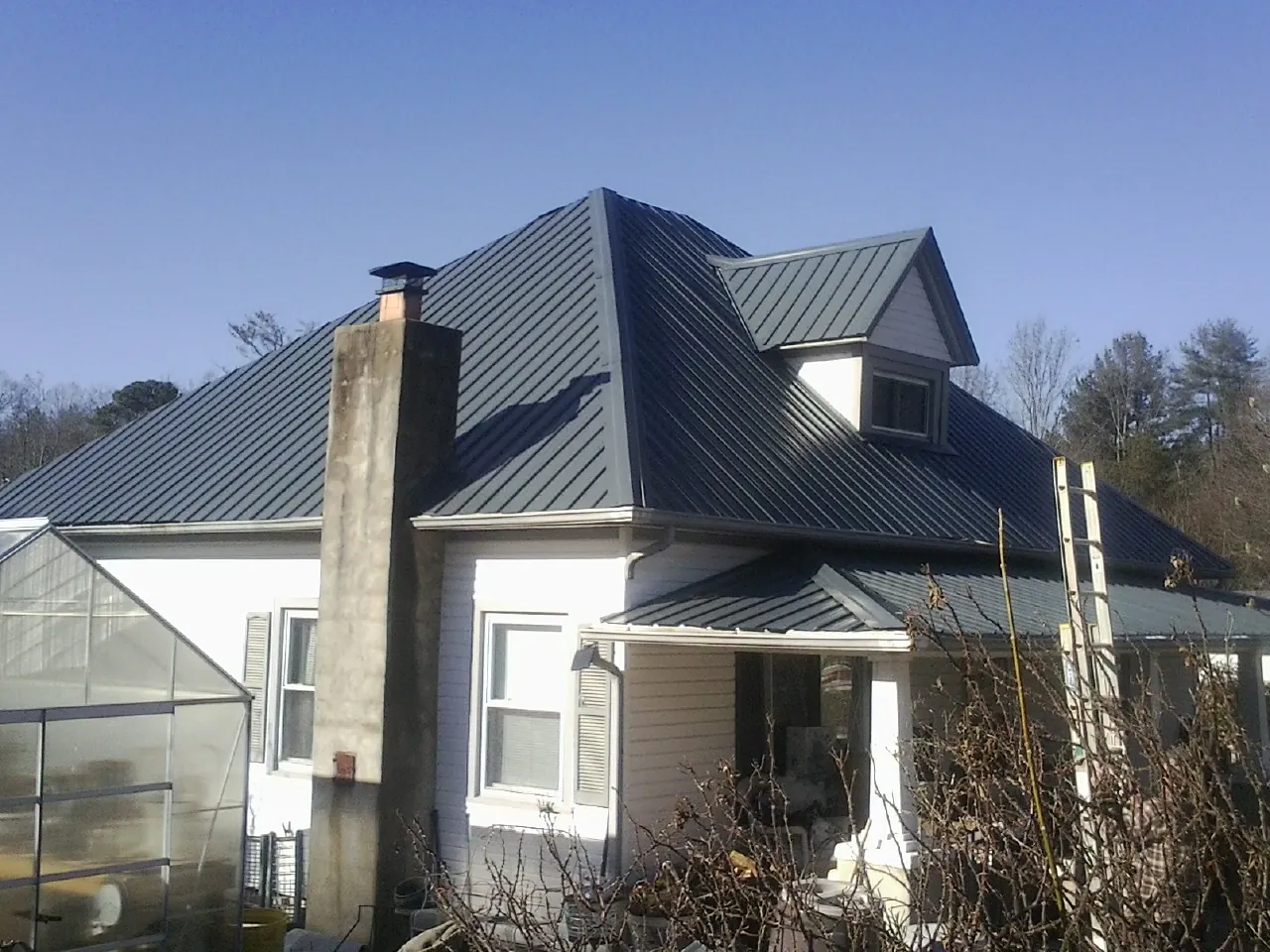 Dark blue standing seam metal roof on a white farmhouse with dormer — Slate & Tile Roof Repair by Roofing Brothers in Parkers Prairie