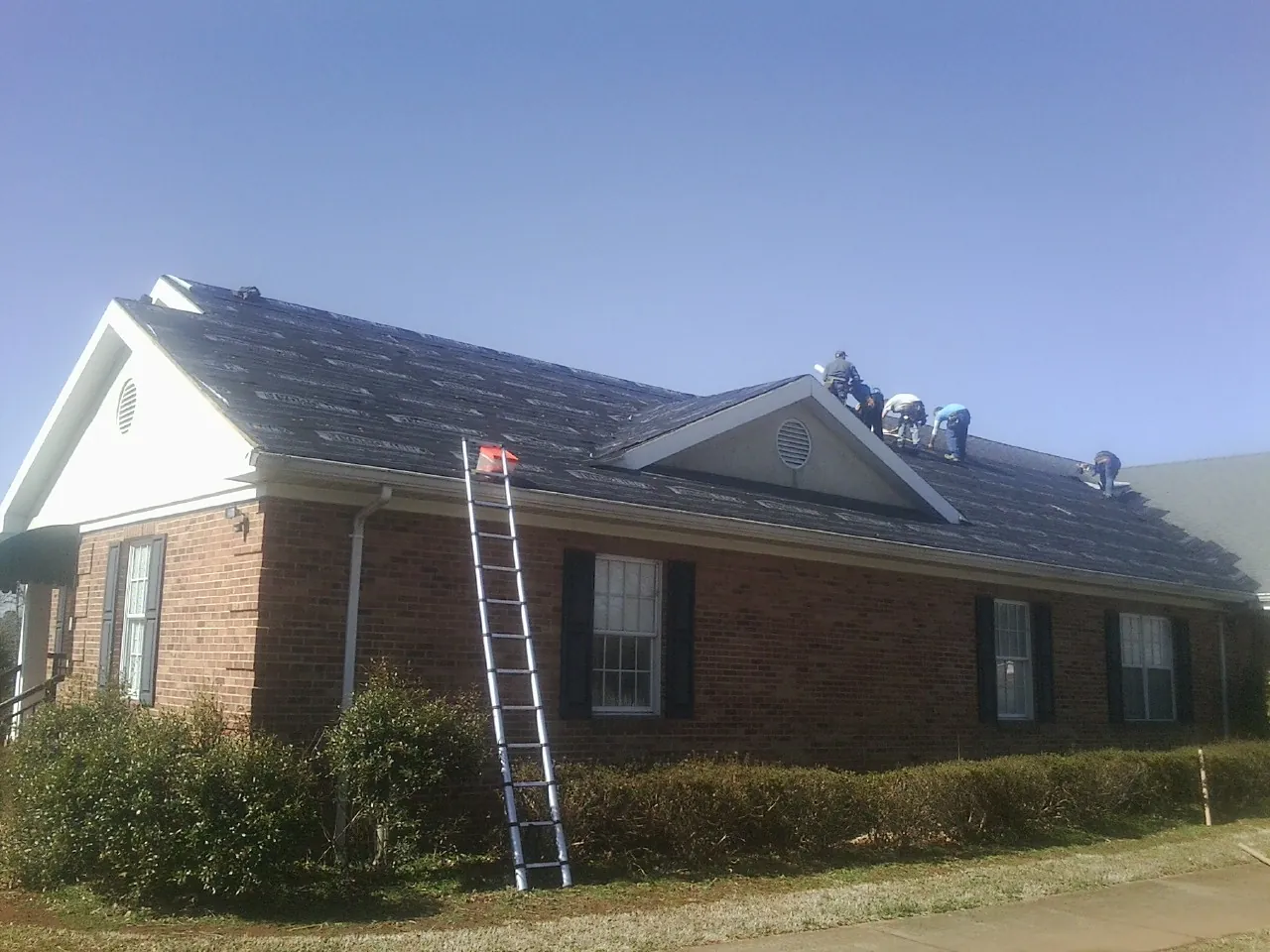 Crew tearing shingles off a brick ranch roof with a ladder set — Metal Roof Repair work by our crew in Parkers Prairie