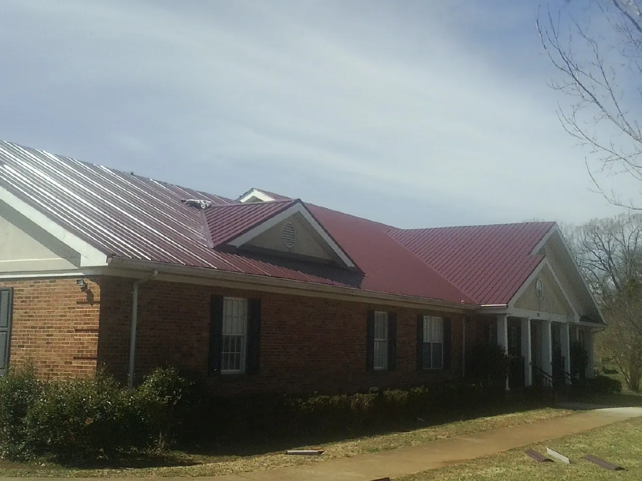 Red metal roof with gabled entries on a long brick building, from a Hail Damage Roof Repair job in Parkers Prairie