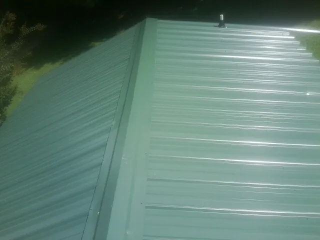 New green metal panels meeting at the ridge of a roof — Flat Roof Repair work by our crew in Parkers Prairie