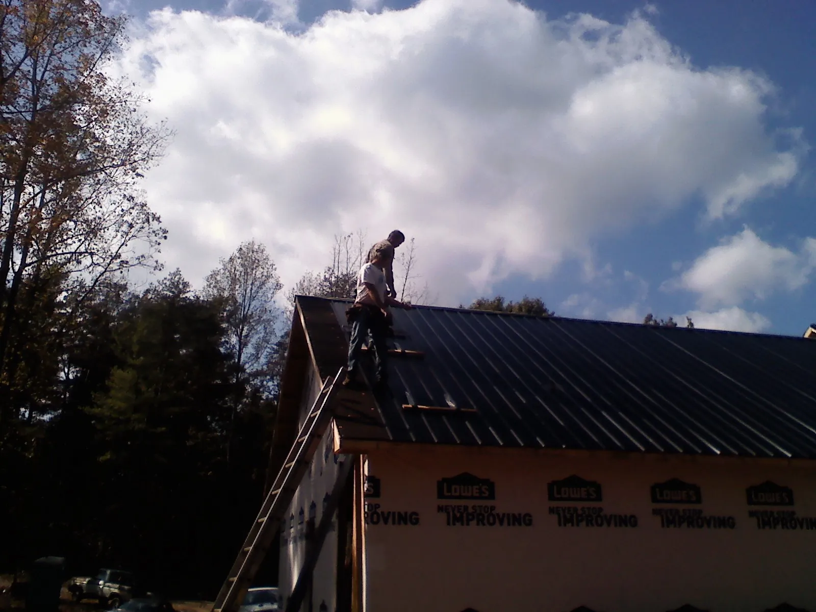 Roofer fastening dark metal panels high against a cloudy sky, from a Roof Inspection job in Parkers Prairie
