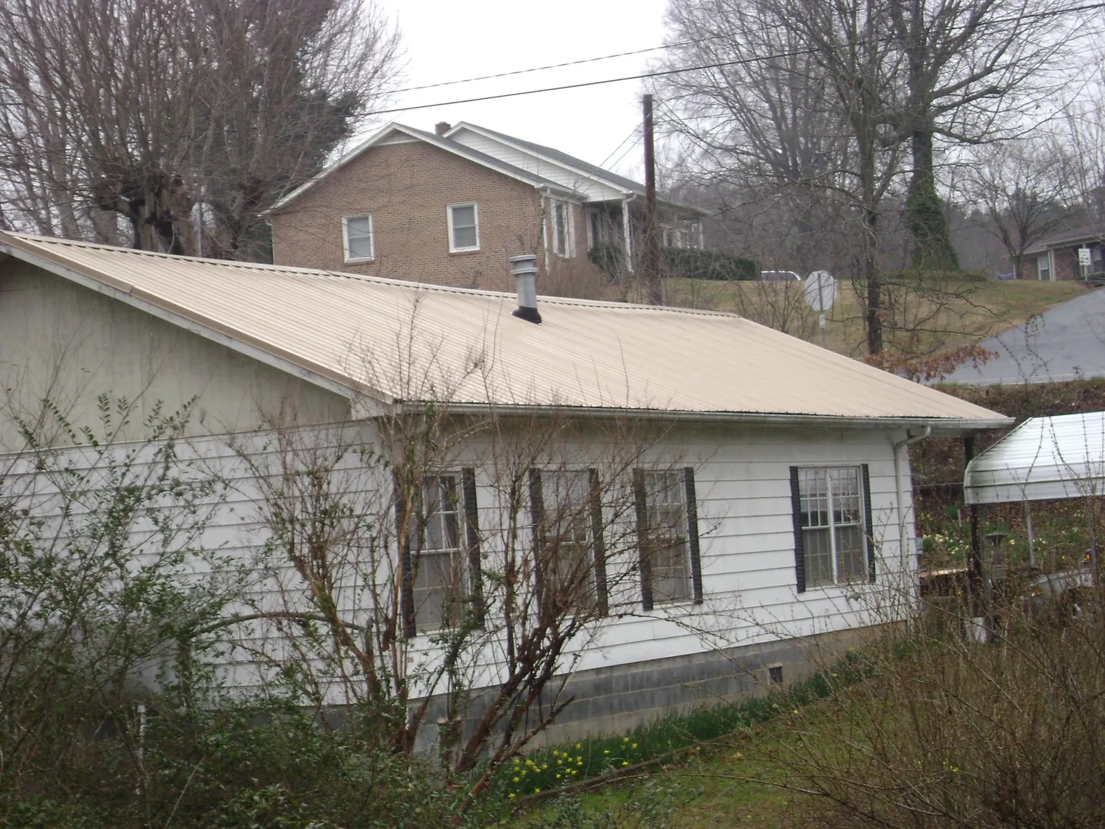 Tan metal roof on a white sided house set into a hillside — Commercial Roofing by Roofing Brothers in Parkers Prairie