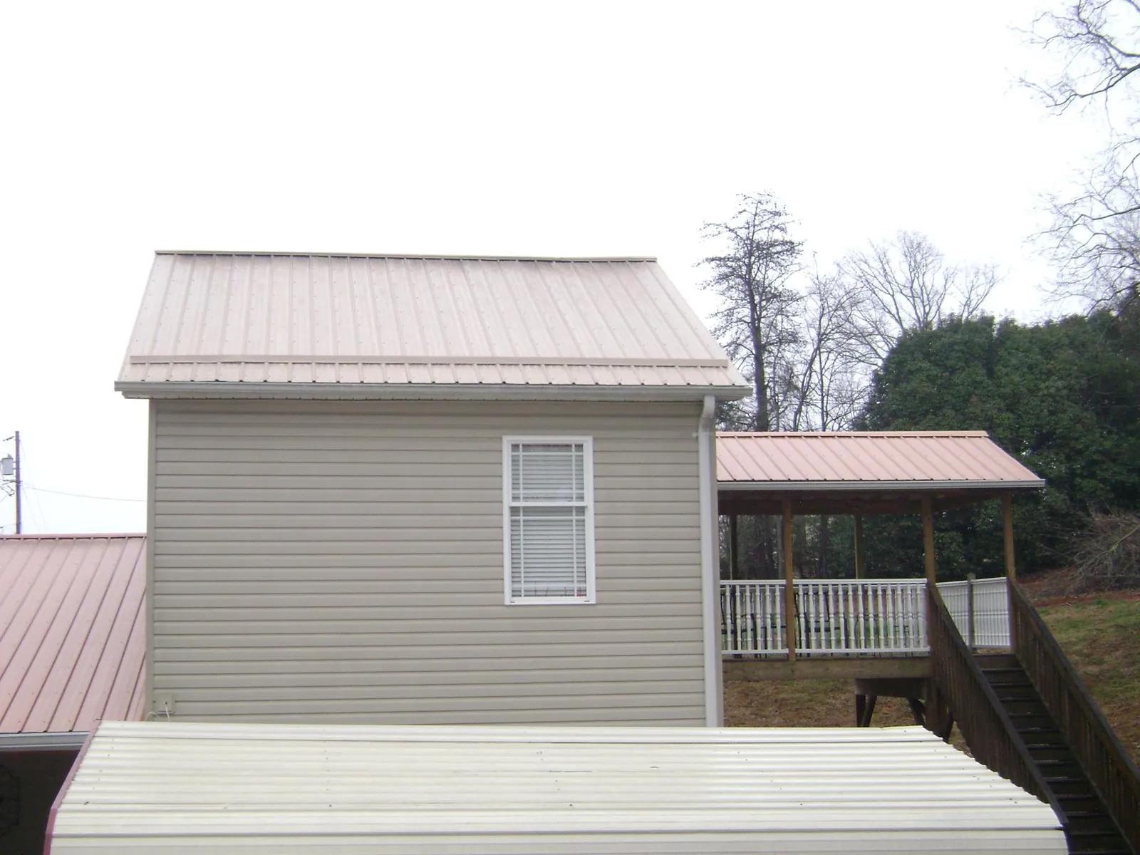 Tan metal roofs on a two story addition and attached porch, from a Roof Replacement job in Parkers Prairie